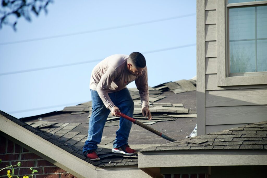 A homeowner examines missing shingles and damaged gutters from the ground after a storm.