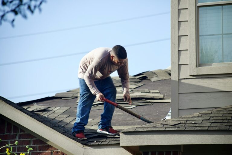 A homeowner examines missing shingles and damaged gutters from the ground after a storm.